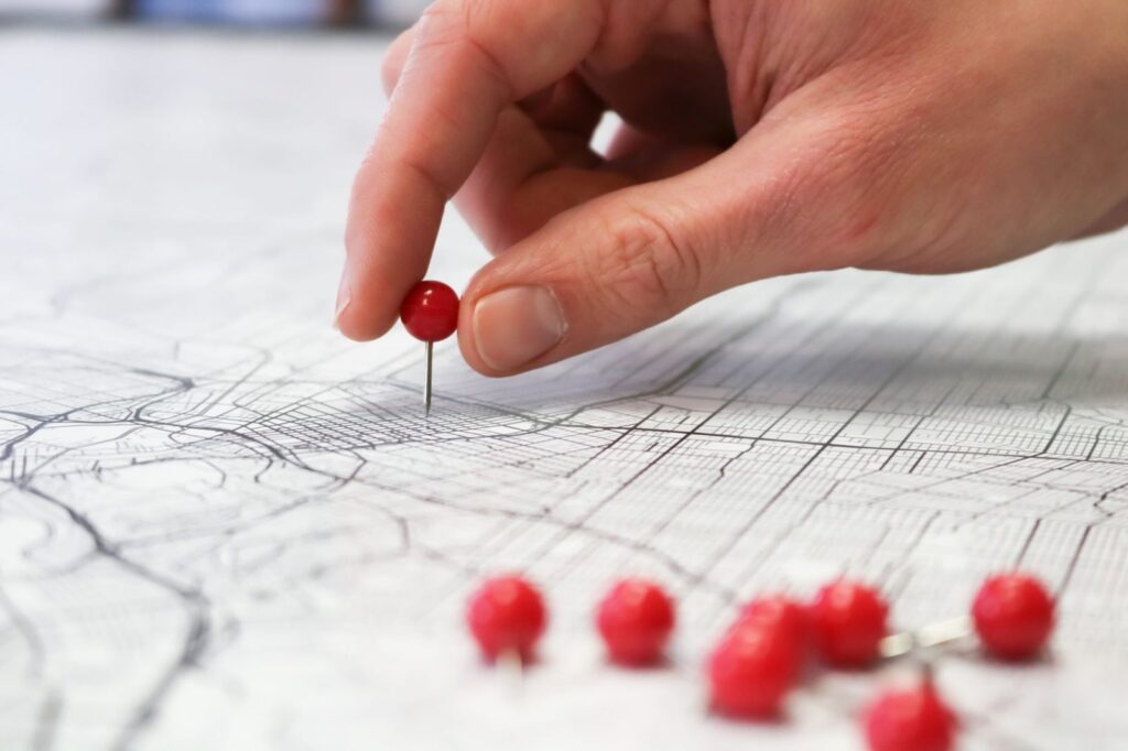Anuncios en Google Maps: tipos, requisitos y cómo empezar 4 Mano clavando una chincheta roja en un mapa: orientar los anuncios a la zona de cada negocio