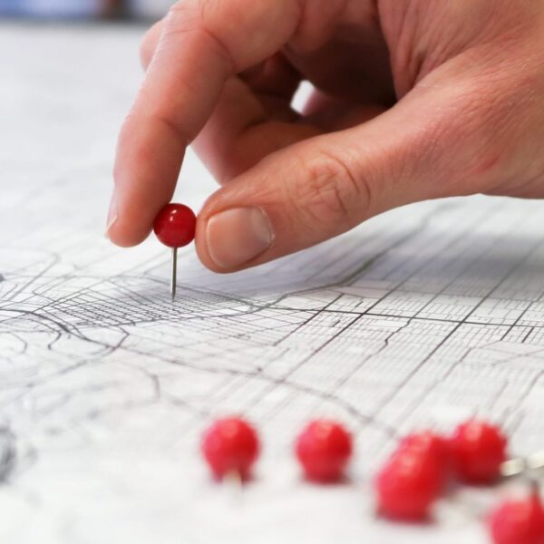Mano colocando chinchetas rojas sobre un mapa: un geogrid mide la posición en Google Maps punto a punto