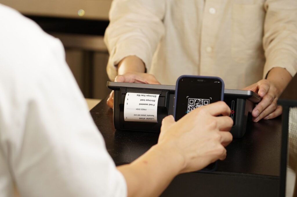 QR y enlace para reseñas de Google: cómo crearlos y dónde ponerlos (2026) 4 Código QR en la pantalla de un móvil junto a la caja de un comercio