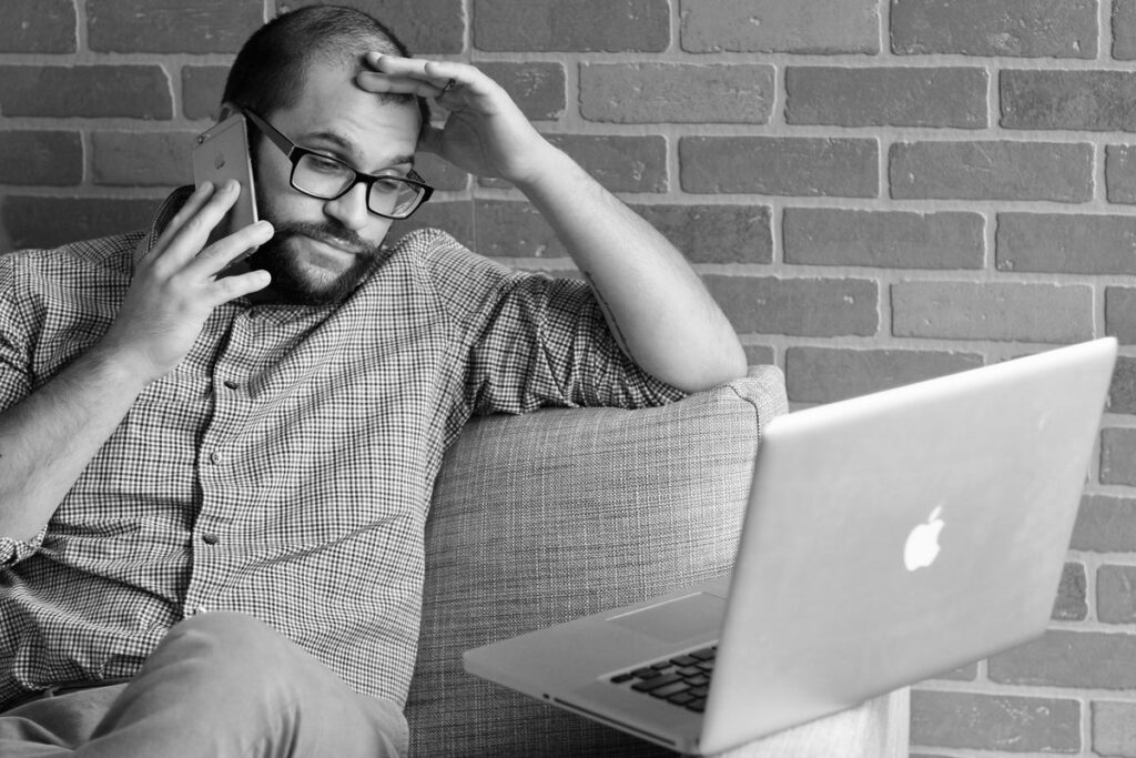 Hombre preocupado hablando por teléfono junto a un portátil: cómo quitar reseñas negativas de Google