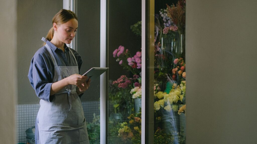 SEO local para franquicias: quién controla las fichas, la web y las reseñas 4 Encargada de una floristería revisando la tableta junto a la cámara de flores: gestionar la ficha de cada local